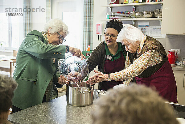 Pflegepersonal unterstützt Senioren beim Kochen im Seniorenheim