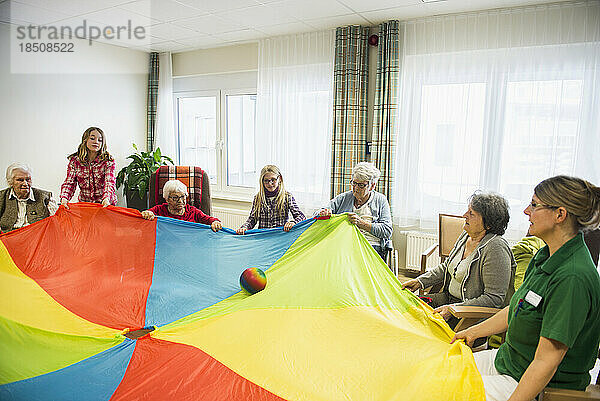 Pflegepersonal mit Mädchen und älteren Frauen bei sportlichen Übungen mit Fallschirm und Ball im Pflegeheim