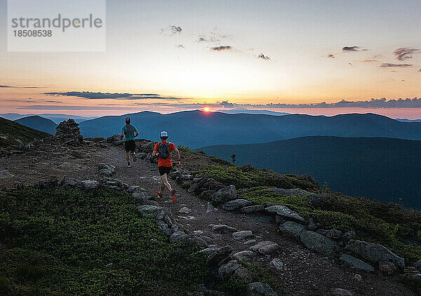 Zwei Trailrunner-Männer laufen bei Sonnenaufgang einen Weg mit Bergen