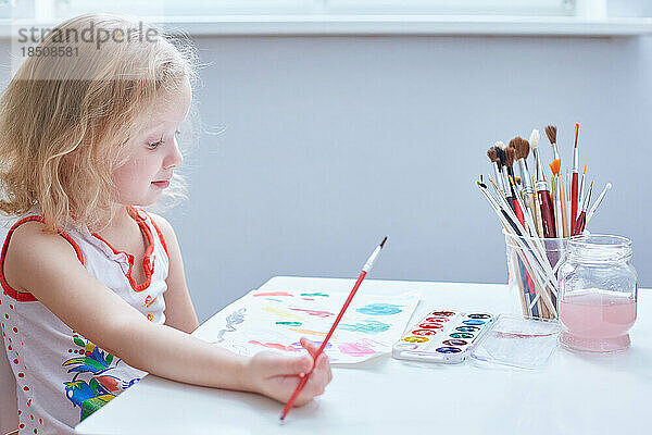 Ein süßes Mädchen mit lockigem Haar malt an einem kleinen Tisch im Kindergarten.