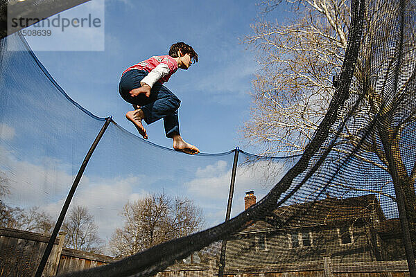 An athletic boy jumps high in trampoline against blue sky