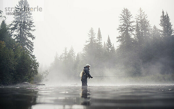 Ein Mann beim Fliegenfischen im Nebel mit Bäumen dahinter