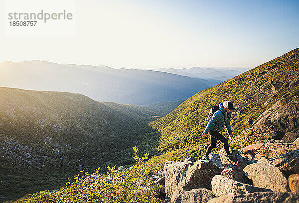 Frau mit Rucksack wandert bei Sonnenaufgang die Felsen im Tal hinauf