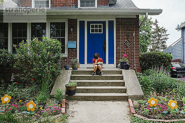 Ein nicht wiederzuerkennendes Kind sitzt auf der Haustür und liest ein Buch