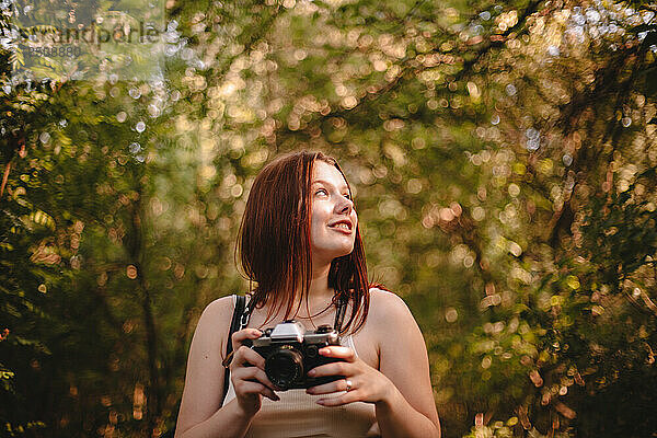 Junge Frau hält Kamera im Wald