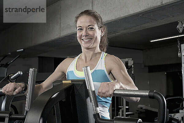 Porträt einer Frau mittleren Alters  die im Fitnessstudio auf einem Trainingsgerät trainiert  Bayern  Deutschland