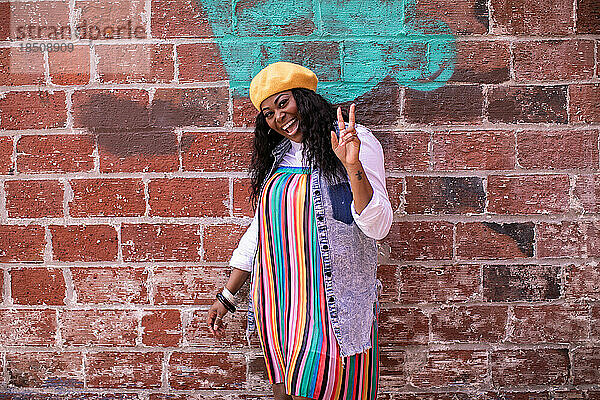 Bunt gekleidete erwachsene schwarze Frau lächelt draußen und zeigt ein Friedenszeichen