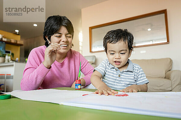 Lateinische Mutter und kleiner Sohn malen gemeinsam von Hand mit Tempera