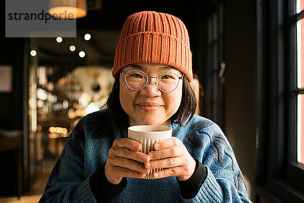 Porträt einer asiatischen Frau  die lächelt und eine heiße Tasse Kaffee hält