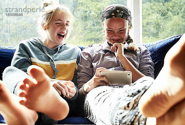 Junge Mädchen sitzen auf einer Couch  schauen auf einen Bildschirm und lachen