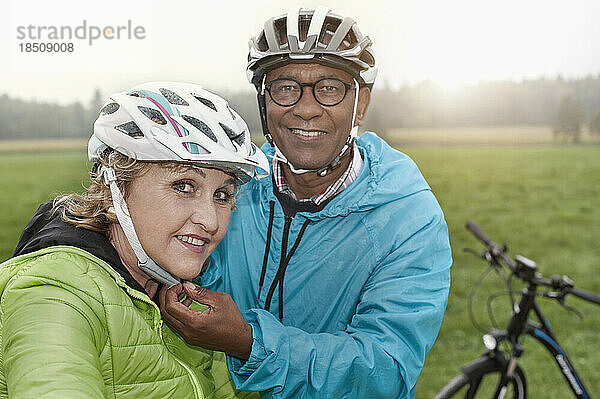 Älterer Mann  der seiner Frau einen Fahrradhelm aufsetzt und lächelt  Bayern  Deutschland