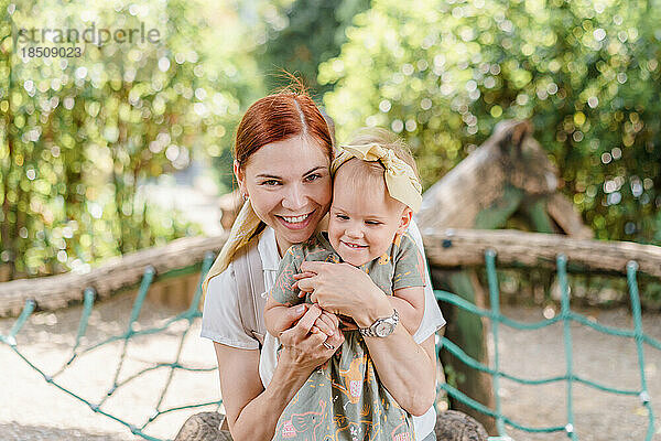 Glückliche Mutter und Kleinkind  die sich auf dem Spielplatz umarmen und lachen