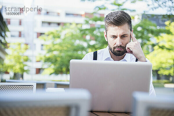 Geschäftsmann arbeitet am Laptop im Straßencafé  München  Bayern  Deutschland