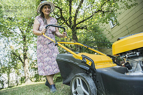 Ältere Frau mäht den Rasen in einem Garten  Altötting  Bayern  Deutschland