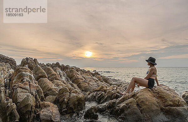 Reisende Frau genießt den Sonnenuntergang allein am felsigen Strand