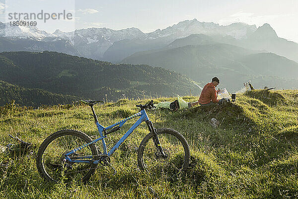 Mountainbiker entspannt sich in alpiner Landschaft und blickt auf die Karte  Bayern  Deutschland