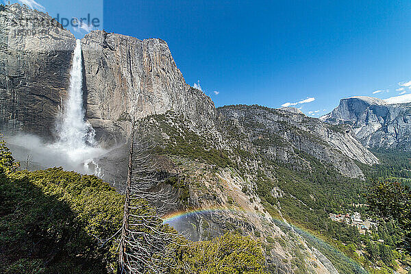 Ein Regenbogen  der sich über das Tal erstreckt und durch einen darüber fließenden Wasserfall entstanden ist