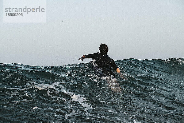 Ein männlicher Surfer paddelt auf trübem Meer