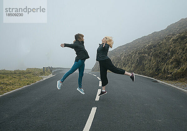 Zwei junge Frauen springen auf einer Straße im Nebel