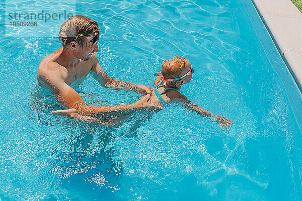 Vater bringt seiner zweijährigen Tochter das Schwimmen im Freibad bei