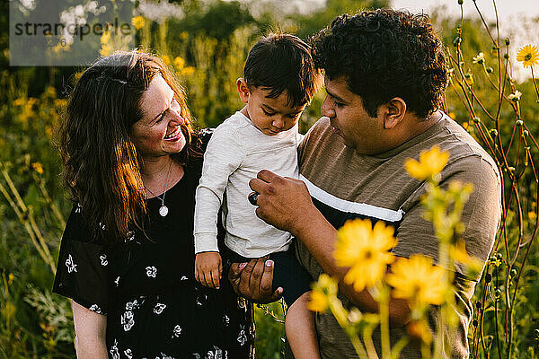 Mama und Papa halten ihr Kleinkind im Blumenfeld im Freien glücklich