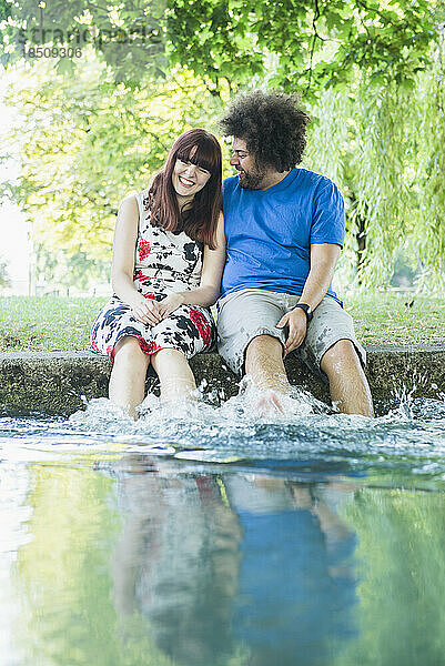 Glückliches Paar sitzt mit Füßen im Wasser am Eisbach