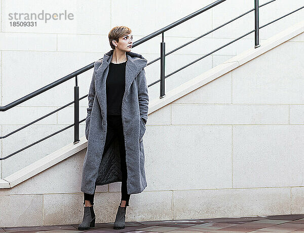 Stilvolle Frau im grauen Mantel blickt auf Treppenhintergrund