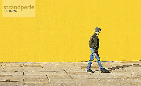 Seitenansicht eines jungen Teenagers  der zu einer gelben Wand geht