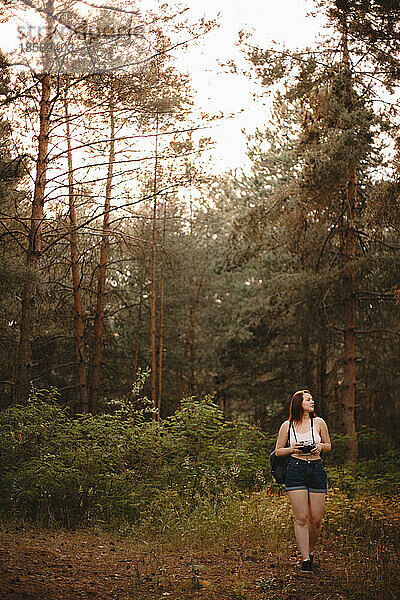 Wanderin mit Kamera spaziert im Sommer im Wald