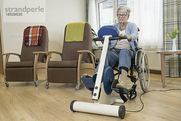 Ältere Frau im Rollstuhl trainiert auf Heimtrainer im Pflegeheim