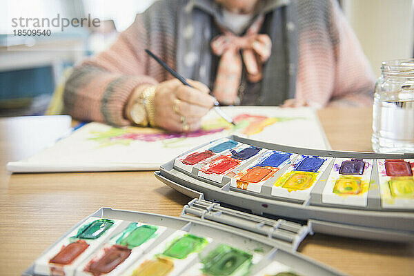 Ältere Frau malt Obst mit Wasserfarbe