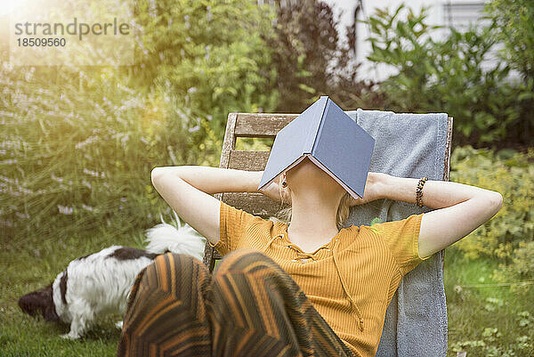 Schöne junge Frau bedeckt ihr Gesicht mit einem Buch und entspannt im heimischen Garten  München  Bayern  Deutschland
