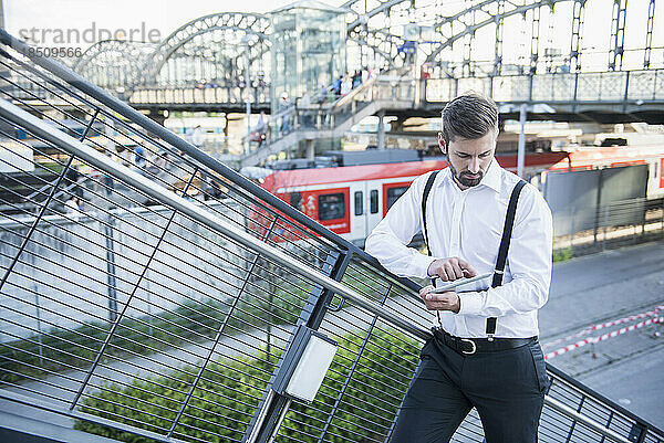 Geschäftsmann steht gegen Geländer und arbeitet an einem digitalen Tablet  München  Bayern  Deutschland