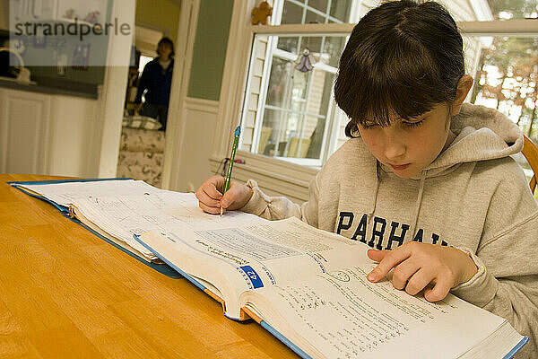 Ein zehnjähriges Mädchen sitzt an ihrem Küchentisch und macht an einem Wochenendnachmittag ihre Hausaufgaben.