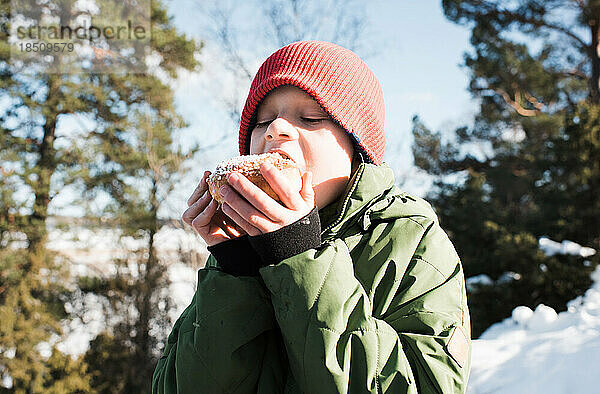 Junge isst einen Kanelbullar  während er draußen in Schweden ist