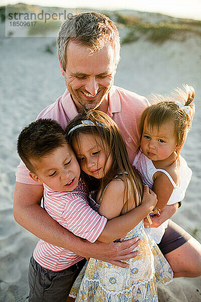 Nahaufnahme eines Vaters  der seine drei Kinder am Strand von San Diego hält