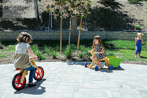 Zwei kleine Mädchen fahren draußen mit hölzernen Laufrädern
