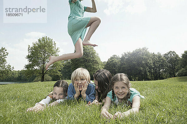 Mädchen springt über ihre auf Gras liegenden Freunde in einem Park  München  Bayern  Deutschland