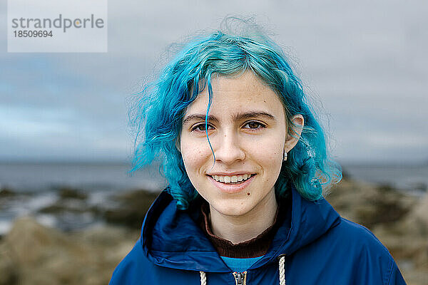 Teenager-Mädchen mit blauen Haaren lächelt an der Küste in die Kamera