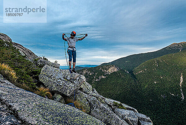 Mann wickelt Seil an der Spitze eines Felsens auf und klettert auf den Berg