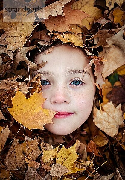 Junges Mädchen lächelt ruhig in einem Haufen Blätter. Herbst-Sprite