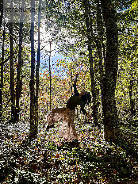 Frau tanzt zwischen Bäumen im Wald