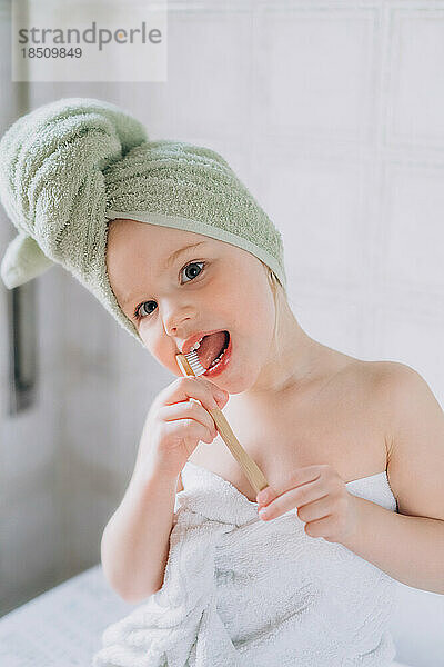 Kleinkind mit einem Handtuch auf dem Kopf putzt Zähne mit einer Bürste