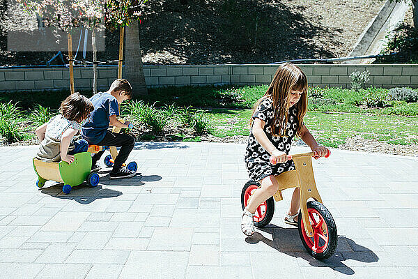 Draußen fahren drei Kinder auf Holzfahrrädern herum