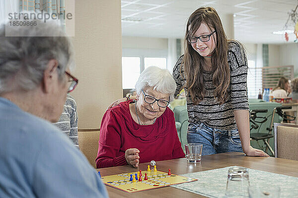 Mädchen spielen Ludo-Brettspiel mit älteren Frauen im Pflegeheim