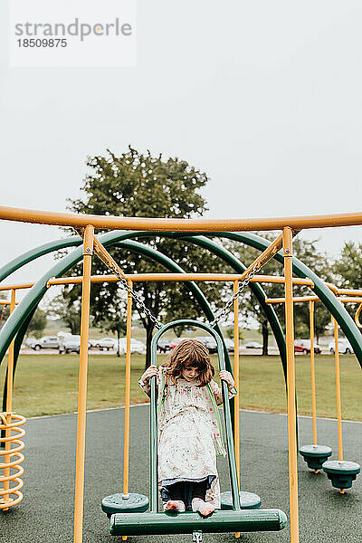 Junges Mädchen spielt an bewölktem Tag auf Spielgeräten im Park