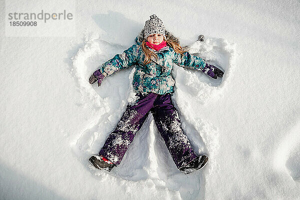 4 Jahre altes Mädchen macht einen Engel im Schnee