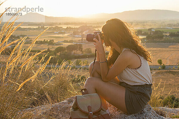 Eine junge Frau macht mit ihrer Kamera ein Foto auf einem Berggipfel