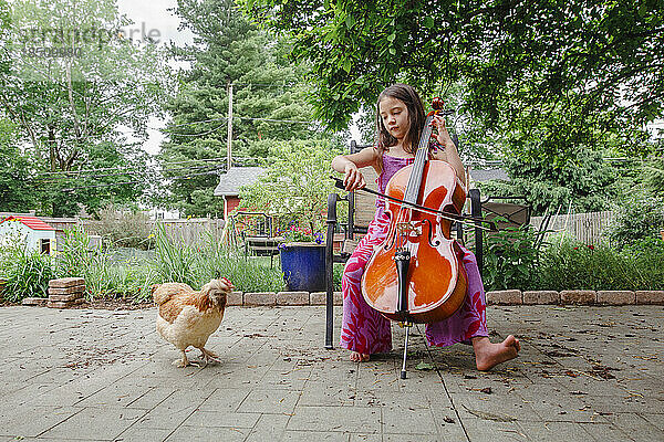 Ein kleines  glückliches Kind spielt draußen ein Cellokonzert für ein Haustierhuhn