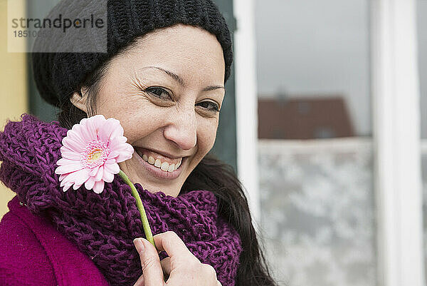 Porträt einer mittleren erwachsenen Frau  die eine rosa Gerbera-Gänseblümchenblume hält und lächelt  Bayern  Deutschland